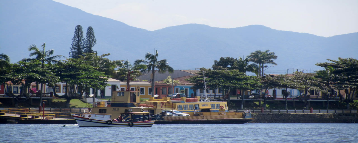 Cidade de Cananéia, com barcos no mar à frente e casas ao fundo. 