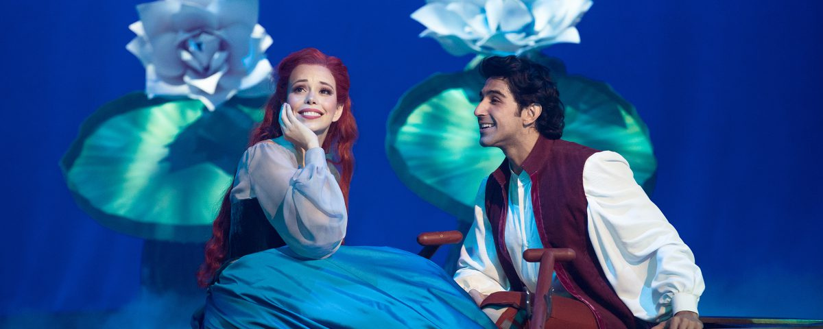 Atriz representando o personagem "A Pequena Sereia" contracena em palco com ator, com fundo azul que remete ao mar. O musical é um dos próximos eventos em São Paulo. 