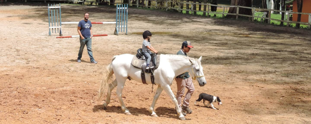 Aula de equitação, com profissional, criança e cavalo na imagem, no Rancho Figueira. 