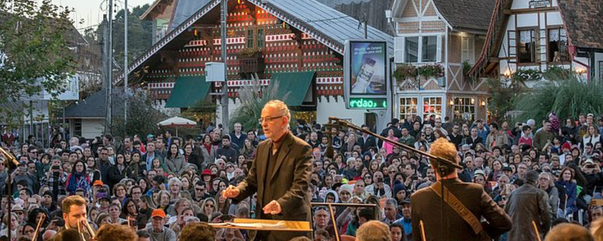 Festival de Inverno de Campos do Jordão em edições passadas, com maestro no palco e público ao fundo. 