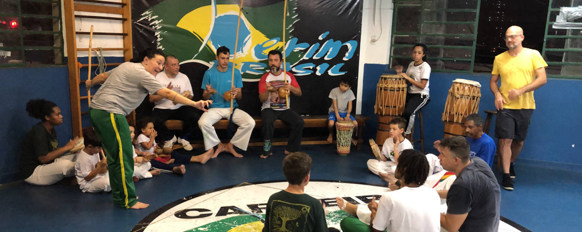 Aulas de capoeira na BerimBrasil, em São Paulo, com roda de alunos no centro. 