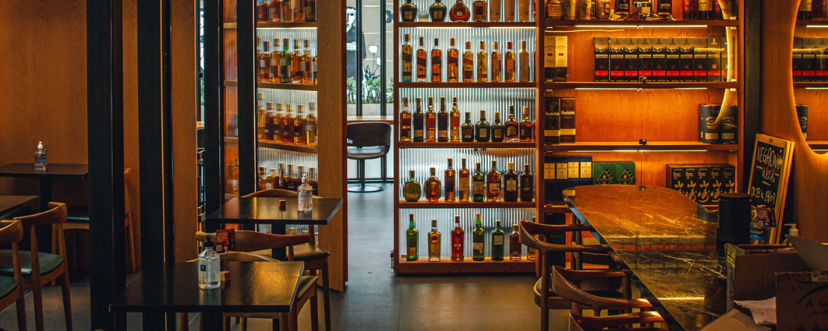 Interior do Caledonia Whisky & Co., com uma adega de whisky, mesas e cadeiras na imagem.