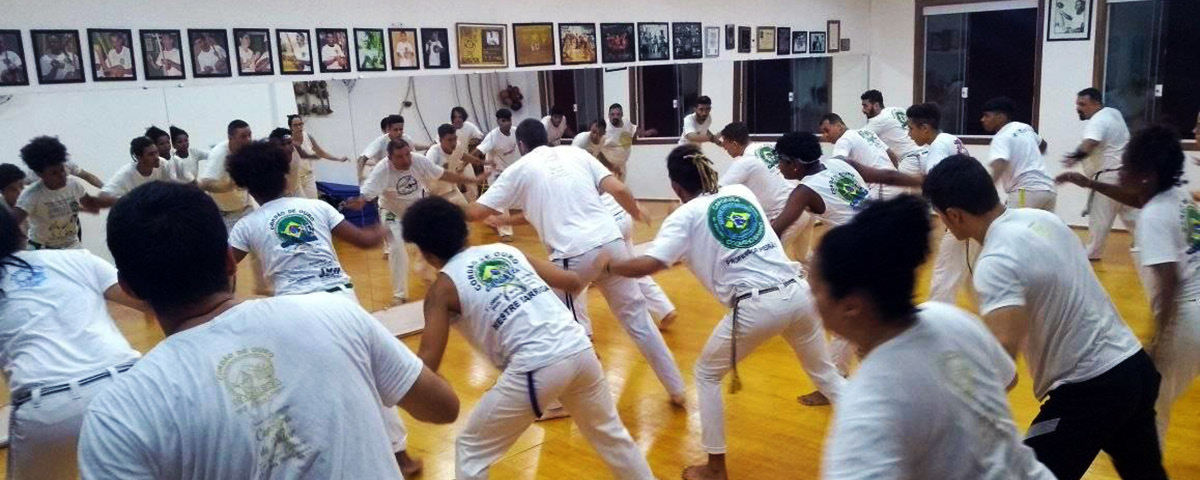 Aulas de Capoeira no Coletivo Mestre da Capoeira de Valor, em Campinas, com vários alunos em uma sala reproduzindo o mesmo movimento. 