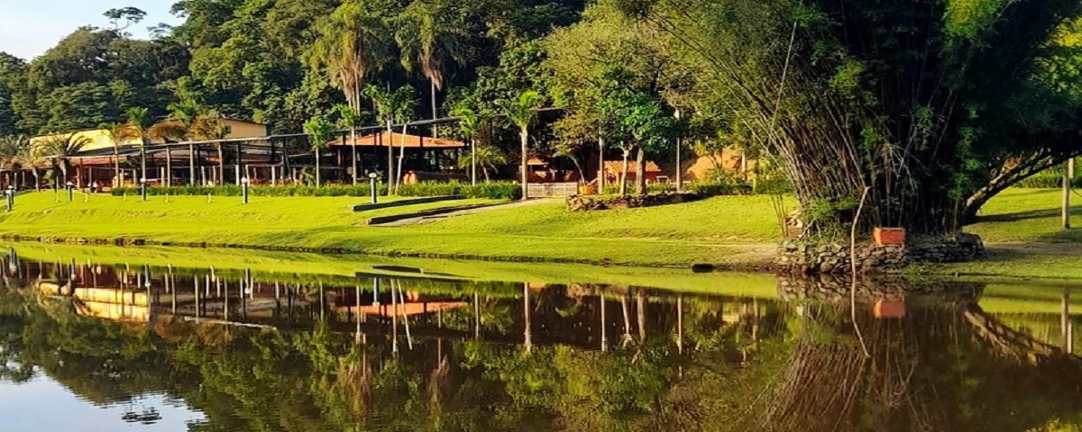 Foto de longe da Estalagem Terra Nova, um dos restaurantes ao ar livre de São Paulo, com árvores e um lago.