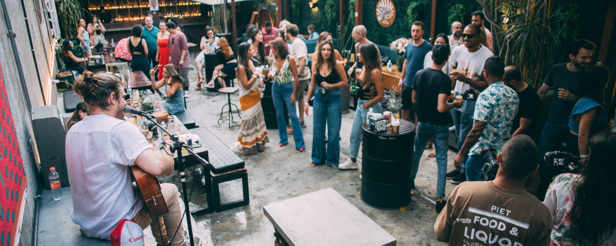 Foto tirada de cima do Iscondido Bar, com um músico e pessoas ao redor conversando e bebendo.