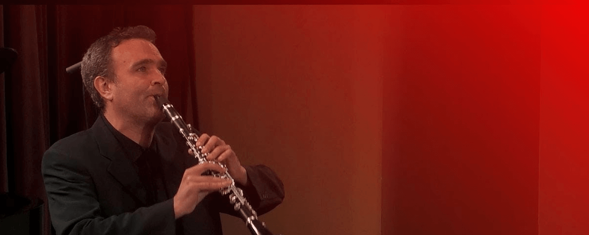Jörg Widmann tocando clarinete com fundo avermelhado. 