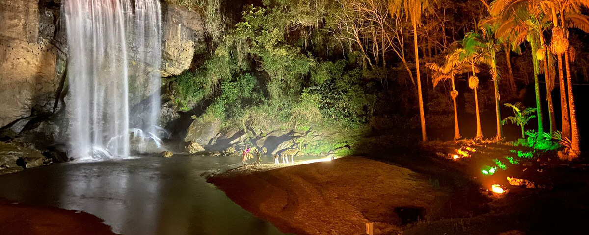 Foto da lagoinha, uma das cachoeiras em São Paulo para se visitar, com luzes em verde e laranja e pessoas tirando fotos.