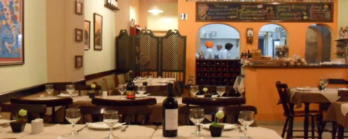 Interior do restaurante Cantina Mamma Celeste, um dos restaurantes no bixiga, com mesas e uma garrafa de vinho sobre uma delas.
