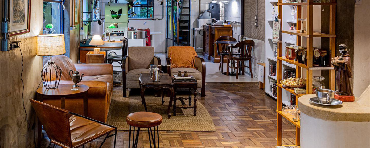 Interior do Coffee Lab, localizado na Vila Mariana, com piso de madeira, sofá de couro marrom, cadeira e outros objetos.  