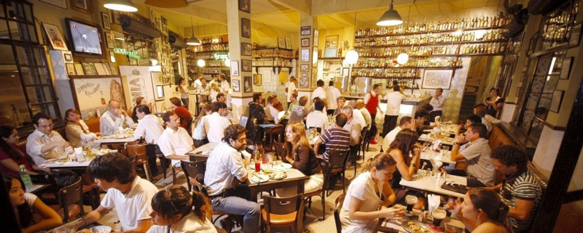 Interior do Bar Pirajá, com diversas pessoas sentadas, bebendo, comendo e conversando.