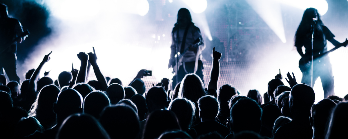 Foto de um show de rock, com os músicos e a plateia em silhueta.