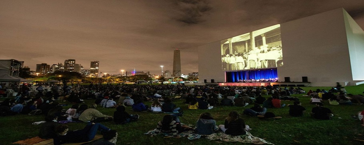 Pessoas sentadas no gramado, assistindo a um filme no Cine Auditório, um dos cinemas ao ar livre de São Paulo, localizado no Ibirapuera.