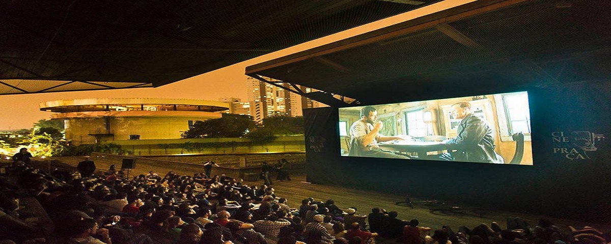 Pessoas sentadas assistindo a um filme no telão do Cine na Praça, um dos cinemas ao ar livre de São Paulo.