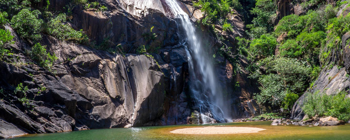 Foto de uma das cachoeiras em São Paulo, com um lago em cor verde e pedras cercadas por vegetação.