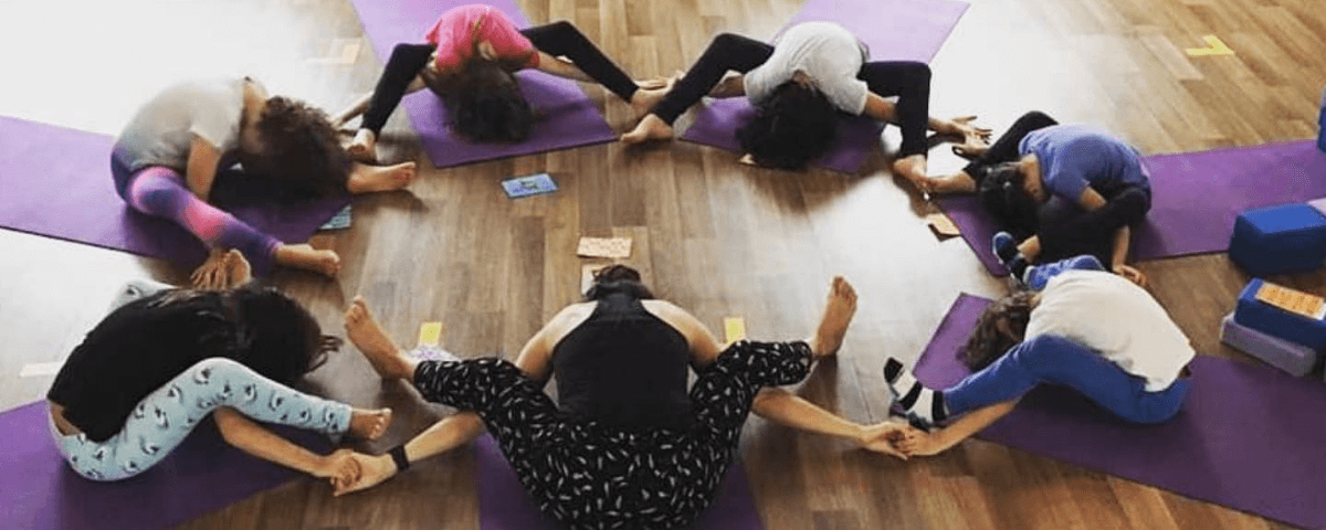 Pessoas sentadas em tapetinhos, uma ao lado da outra, formando um círculo, praticando hot yoga.