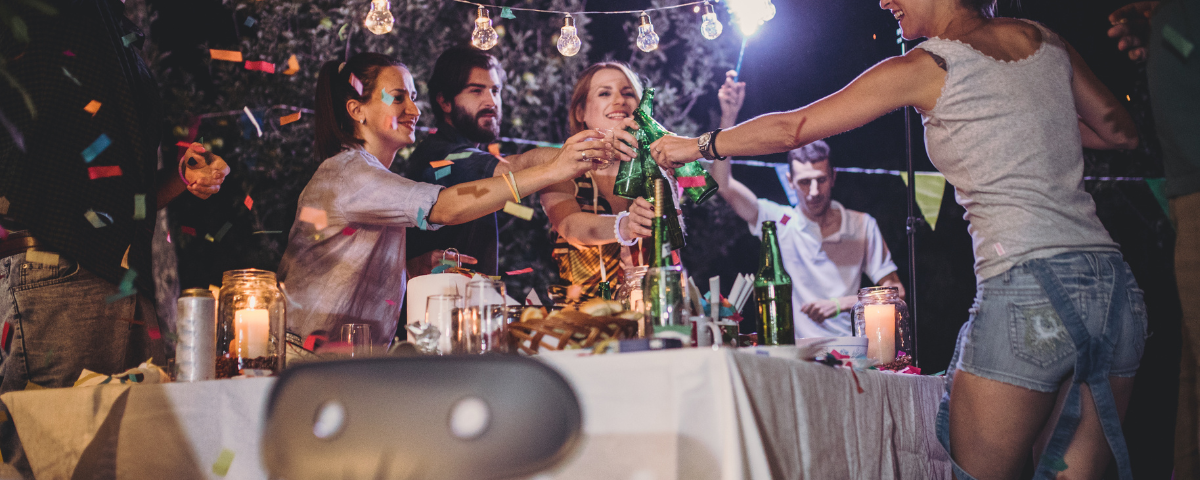 Pessoas fazendo um brinde com cervejas sobre uma mesa de aniversário.