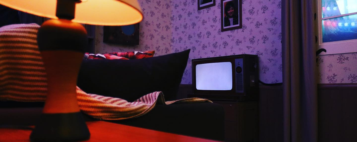 Foto do de uma das salas do Escape 60, com um papel de parede, televisão e abajur.