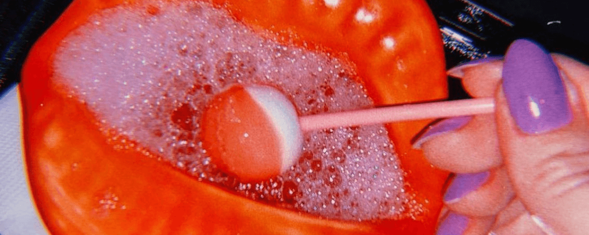 Foto de um dos drinks do Caulí Lounge Bar, com uma mão segurando um pirulito vermelho dentro do copo.