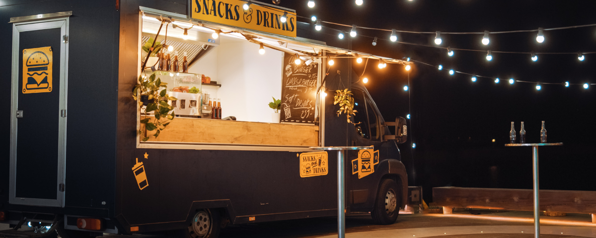 Food Truck preto de bebidas e comidas estacionado, com luzes penduradas.