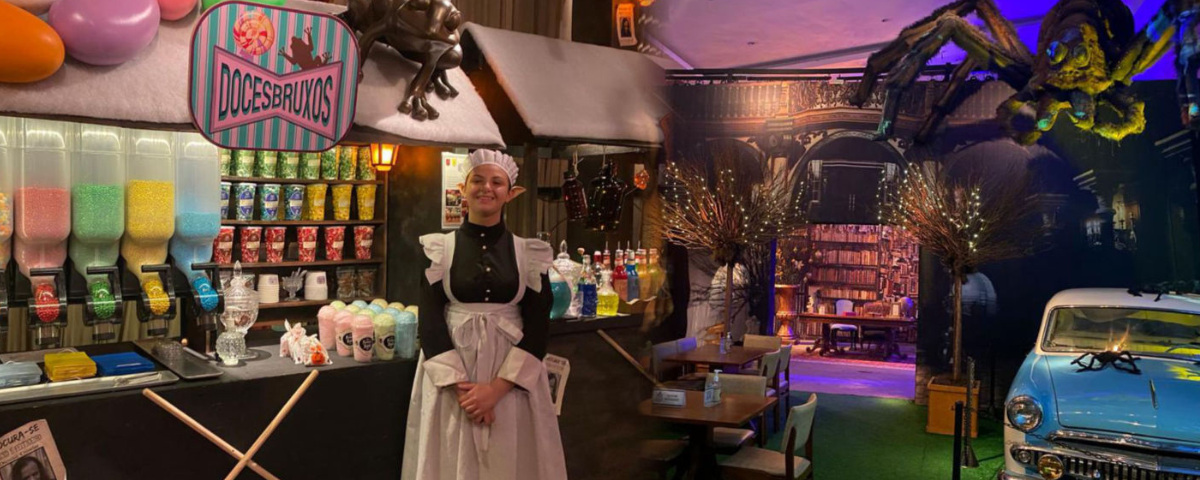 Interior do Magia & Bruxaria Restaurante, com uma mulher vestida de aldeã, com máquinas de doces ao fundo.