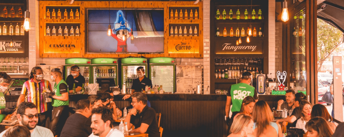 Interior do O Pasquim Bar e Prosa, um dos bares para ir em São Paulo, com pessoas sentadas e em pé, conversando, dando risada e bebendo.