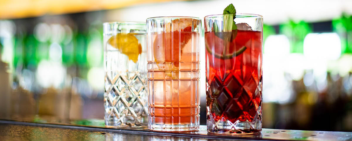 Foto de 3 copos com drinks vermelho, laranja e transparente do Amiiici Lounge.