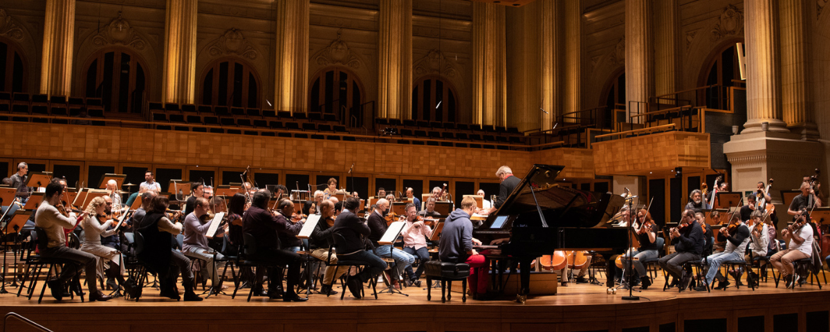 Foto da Orquestra Sinfônica do Estado de São Paulo se apresentando em um dos seus espetáculos, com pessoas tocando instrumentos clássicos.
