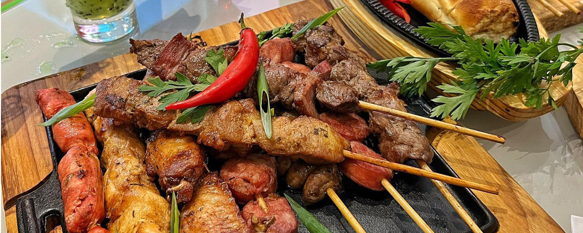 Rodízio de espeto com diversas opões sobre a mesa, de carne, linguiça, frango e pimenta vermelha sobre a mesa.