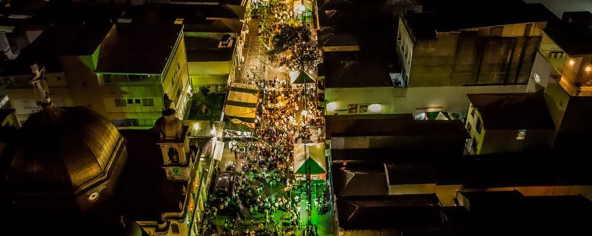 Foto de tirada de cima da Festa de Nossa Senhora da Achiropita, com diversas pessoas juntas e com luzes em verde e amarelo.