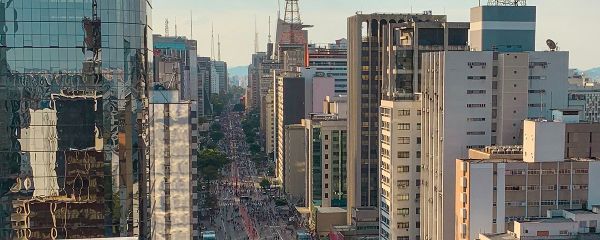 Foto da Av. Paulista, clássica e tradicional do bairro da Bela Vista, com pessoas juntas passeando pela avenida e prédios ao redor.