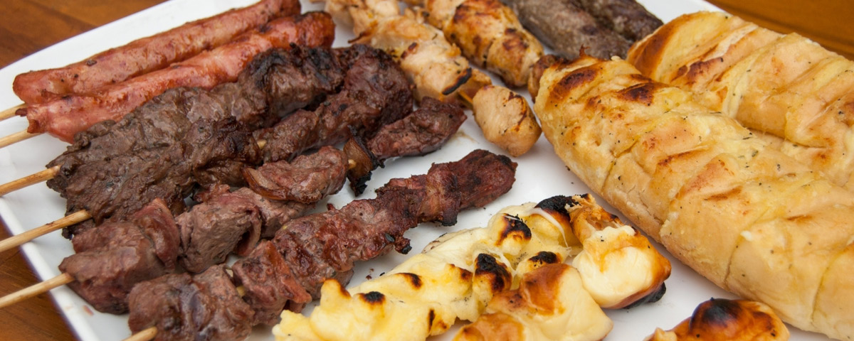 Espetinhos de carne, linguiça, frango e pão de alho sobre um prato.