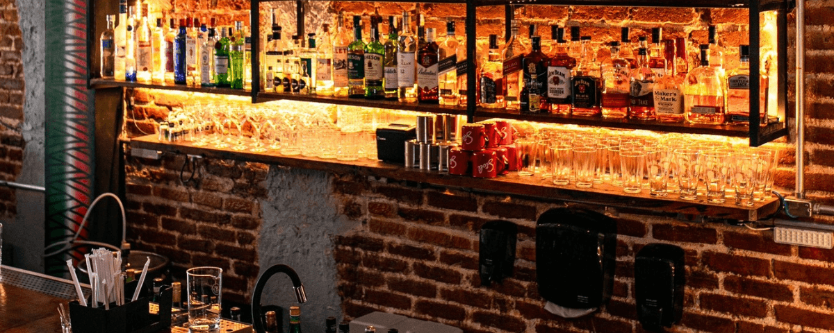 Imagem do interior da parte do bar do Bottega 21, com diversas garrafas de bebidas e uma parede de tijolinhos.