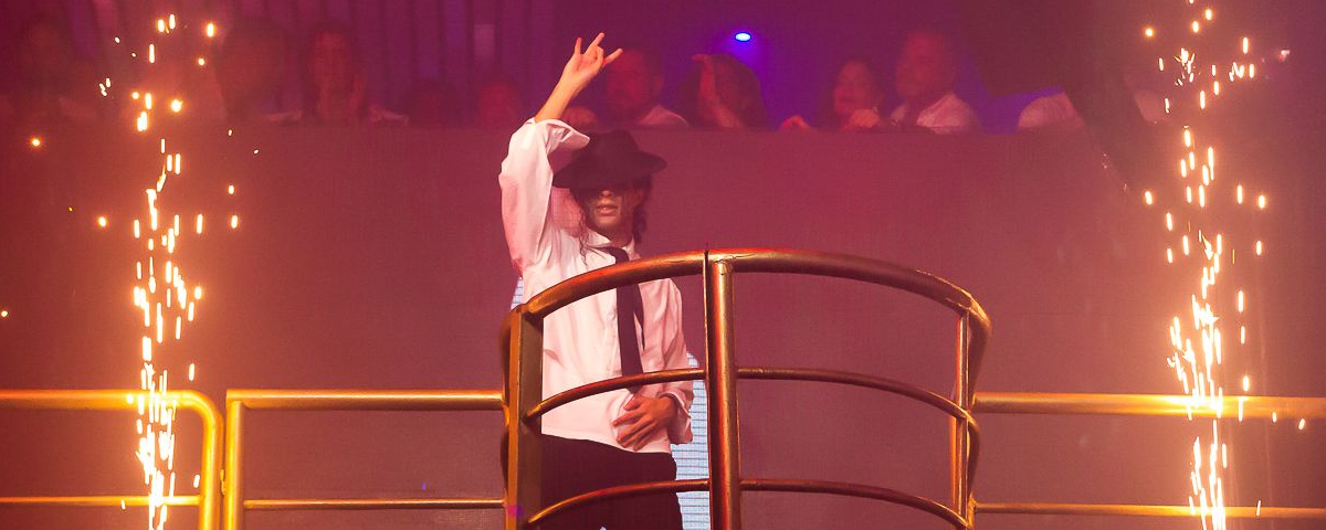 Homem com chapéu, dançando com uma mão estendida para o alto.