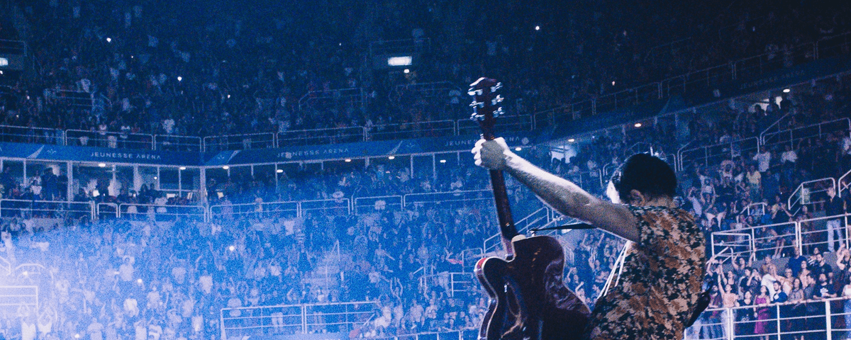 Vocalista do Skank Samuel Rosa toca sua guitarra para uma multidão durante show. 