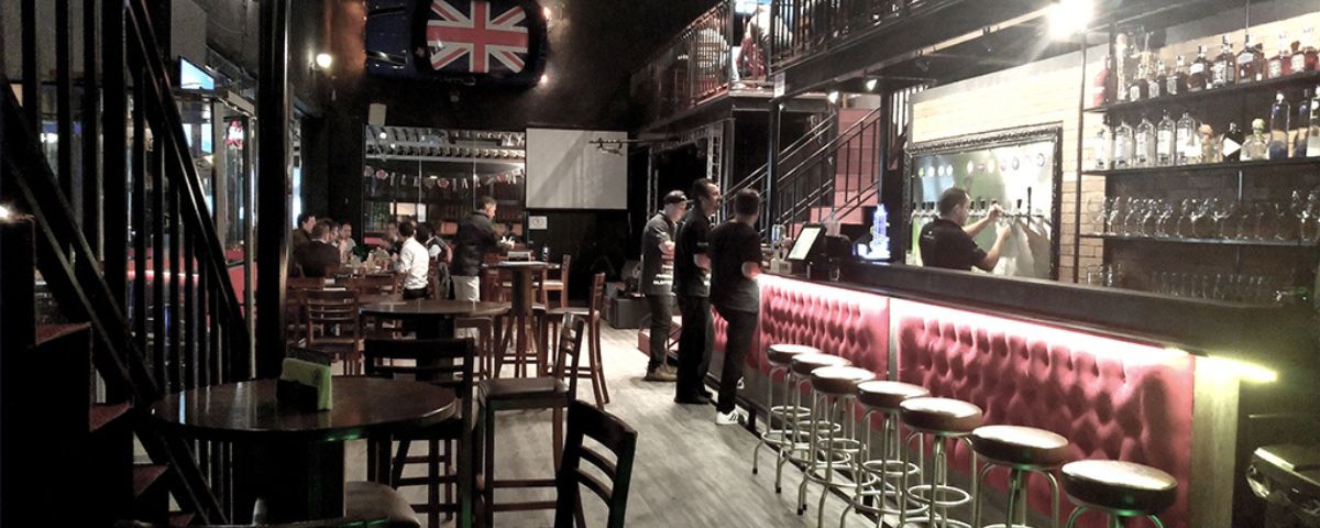 O bar Old Town English Pub tem mesas e cadeiras de madeira espalhas e uma bancada no bar com banquetas para sentar. 