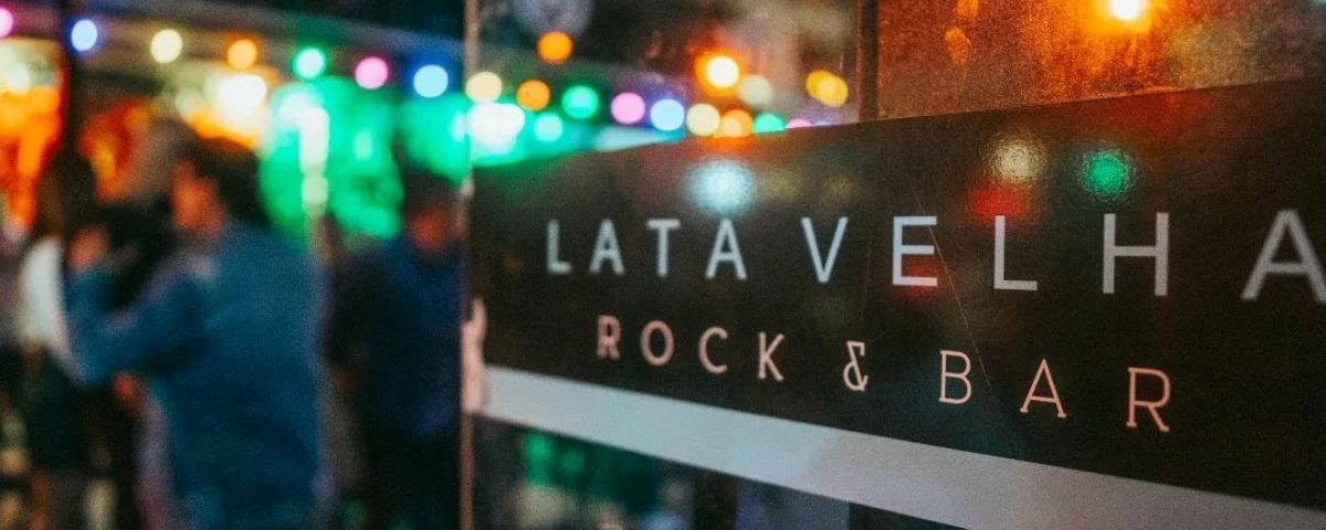 O bar de rock Lata Velha tem shows, transmissões de partidas de futebol e UFC e muito mais. O nome do local está escrito em faixa colada em porta de vidro. 