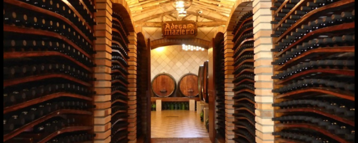 Um dos passeios em Jundiaí, a adega Maziero tem muitas garrafas de vinho expostas nas laterais e ao fundo dois barris para a produção da bebida.