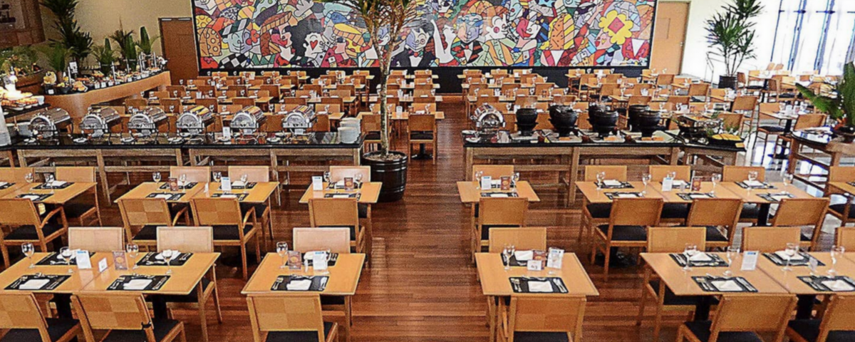 Neste Dia das Mães 2023, o restaurante do Hotel Holiday Inn, com um espaço cheio de cadeiras e mesas com tonalidades marrons, irá ter um almoço especial. 