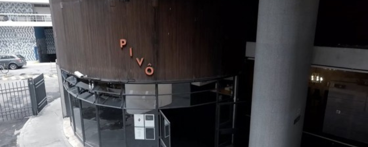 A Pivô, uma galeria em SP, tem na sua fachada vidros e um painel marrom com o nome da galeria em letras na diagonal escritas na cor laranja. 
