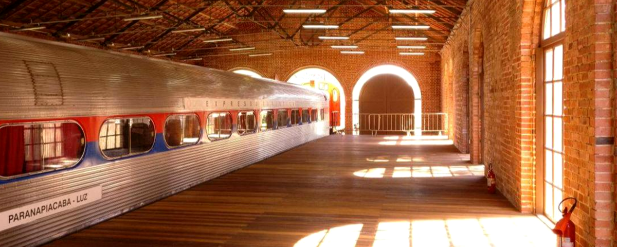 Estação de trem feita de tijolos com trem prateado com o nome do destino: Paranapiacaba. 