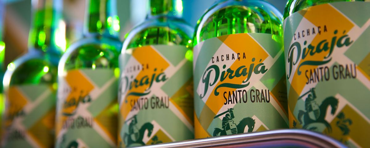 Várias garrafas de cachaça com rótulo colorido em verde e amarelo com o nome do Bar Pirajá. 