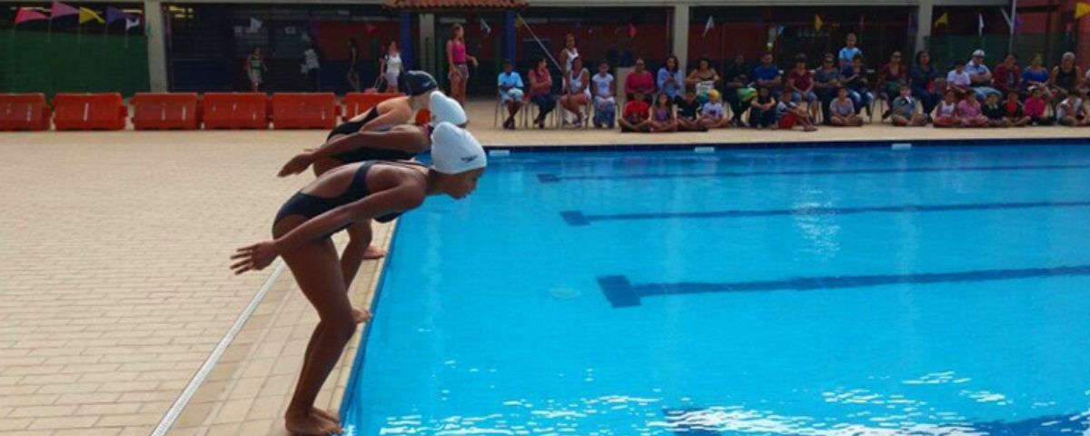 Meninas se preparam para pular na piscina usando tocas e maiôs apropriados para praticar natação. 