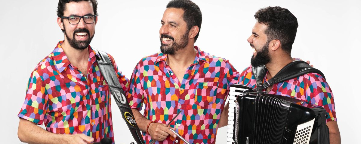 O Sesc Belenzinho está com uma programação incrível em junho. Trio musical com sanfona sorri, usando uma camisa estampada igual. 