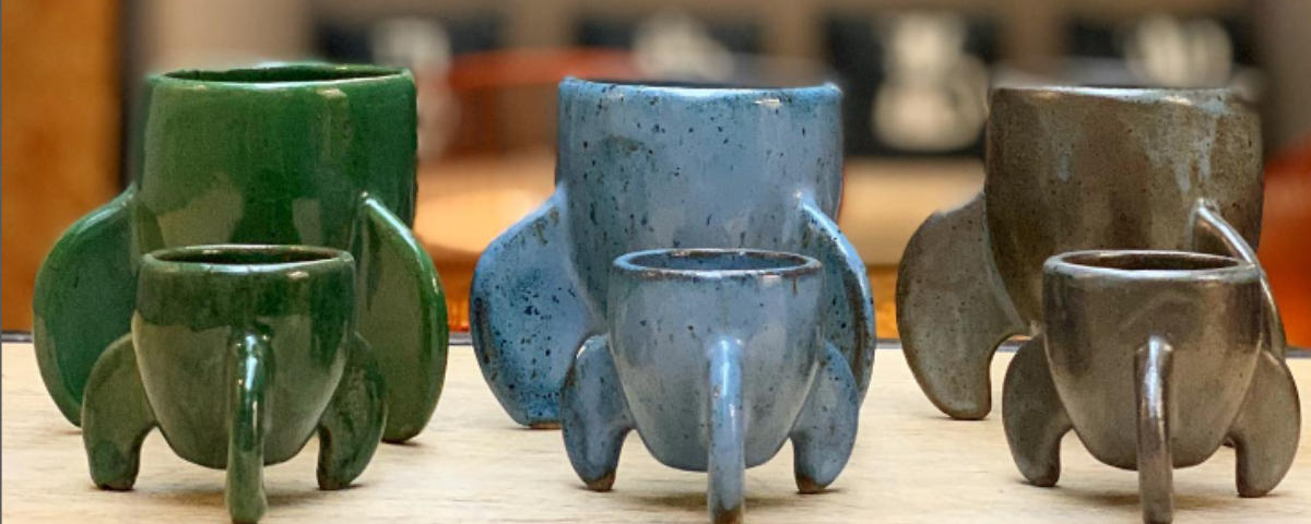 Três xícaras em formato de foguete, nas cores verde, azul e cinza, respectivamente da esquerda para a direita. 
