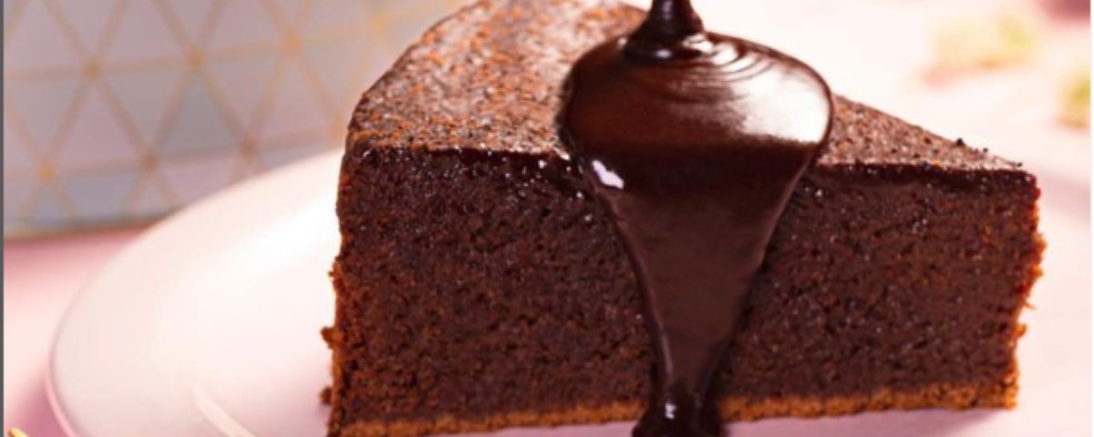 Fatia de bolo de chocolate com calda sendo derramada em cima. 