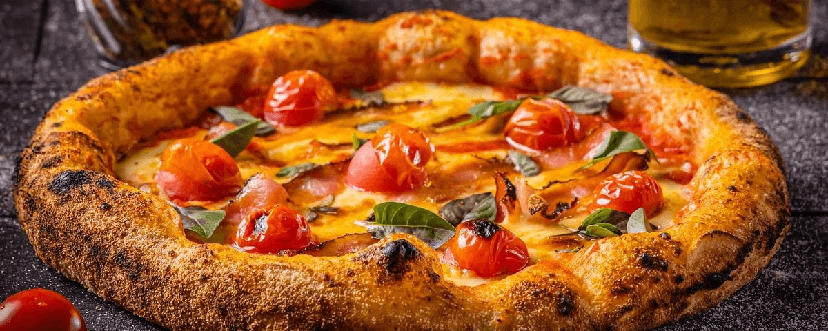Pizza com crosta dourada, queijo, tomatinhos e folhas de manjericão que é servida na Pizza da Mooca. Partiu comemorar o Dia da Pizza em SP? 