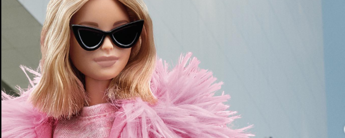 Boneca da Barbie usa roupa cor-de-rosa e óculos escuros. O JK Iguatemi traz um evento em SP onde é possível fazer uma imersão na casa da Barbie em tamanho real. 