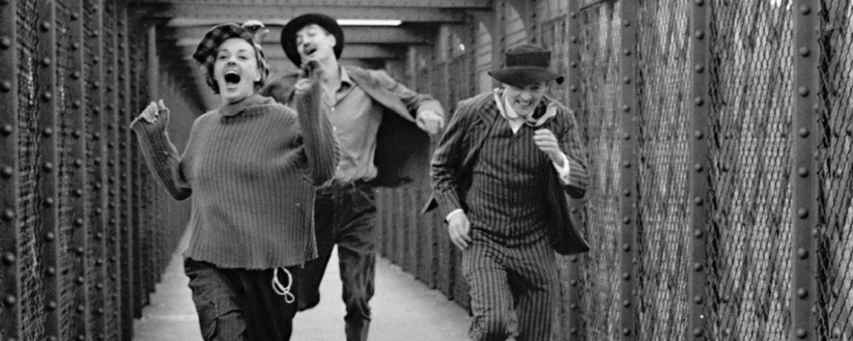 Cena do filme Filme Jules e Jim – Uma Mulher Para Dois, em preto e branco, onde uma mulher e dois homem correm.