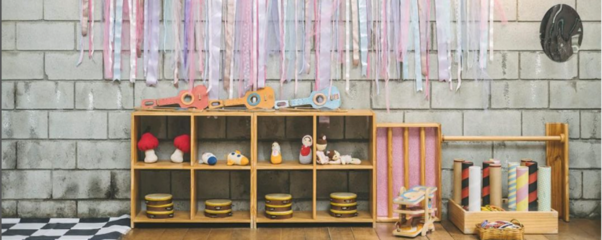 A brinquedoteca em SP chamada Mamusca tem um espaço lúdico com fitas cor-de-rosa penduradas na parede, pequenos violões para as crianças brincarem e outros brinquedos para interação. 