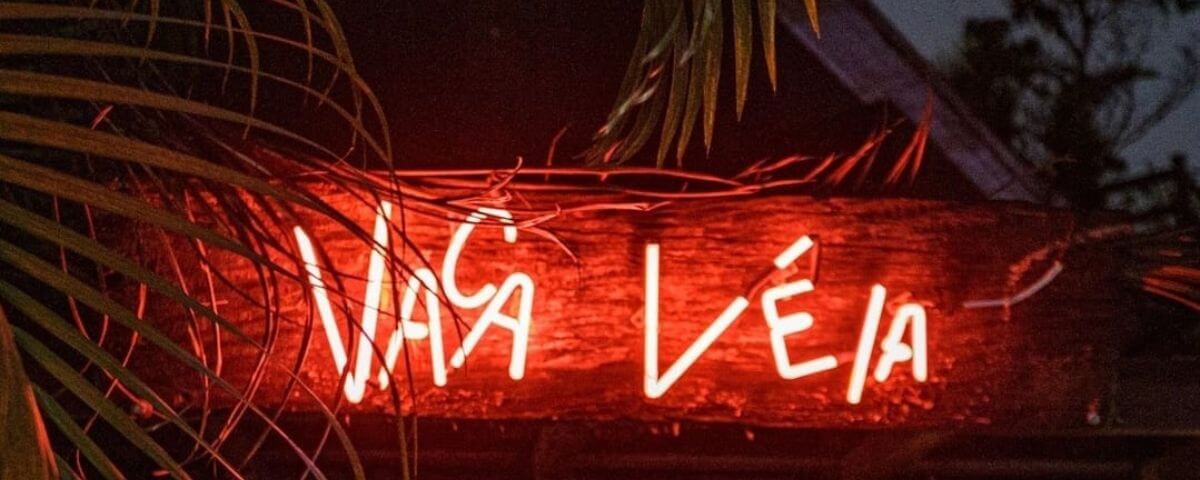 Letreiro vermelho iluminado tem o nome do bar "Vaca Véia" escrito. 